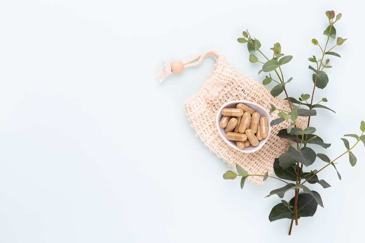 Doplňky stravy pro ženy na bílém pozadí, označená jako vitamíny pro hormonální rovnováhu a energii.